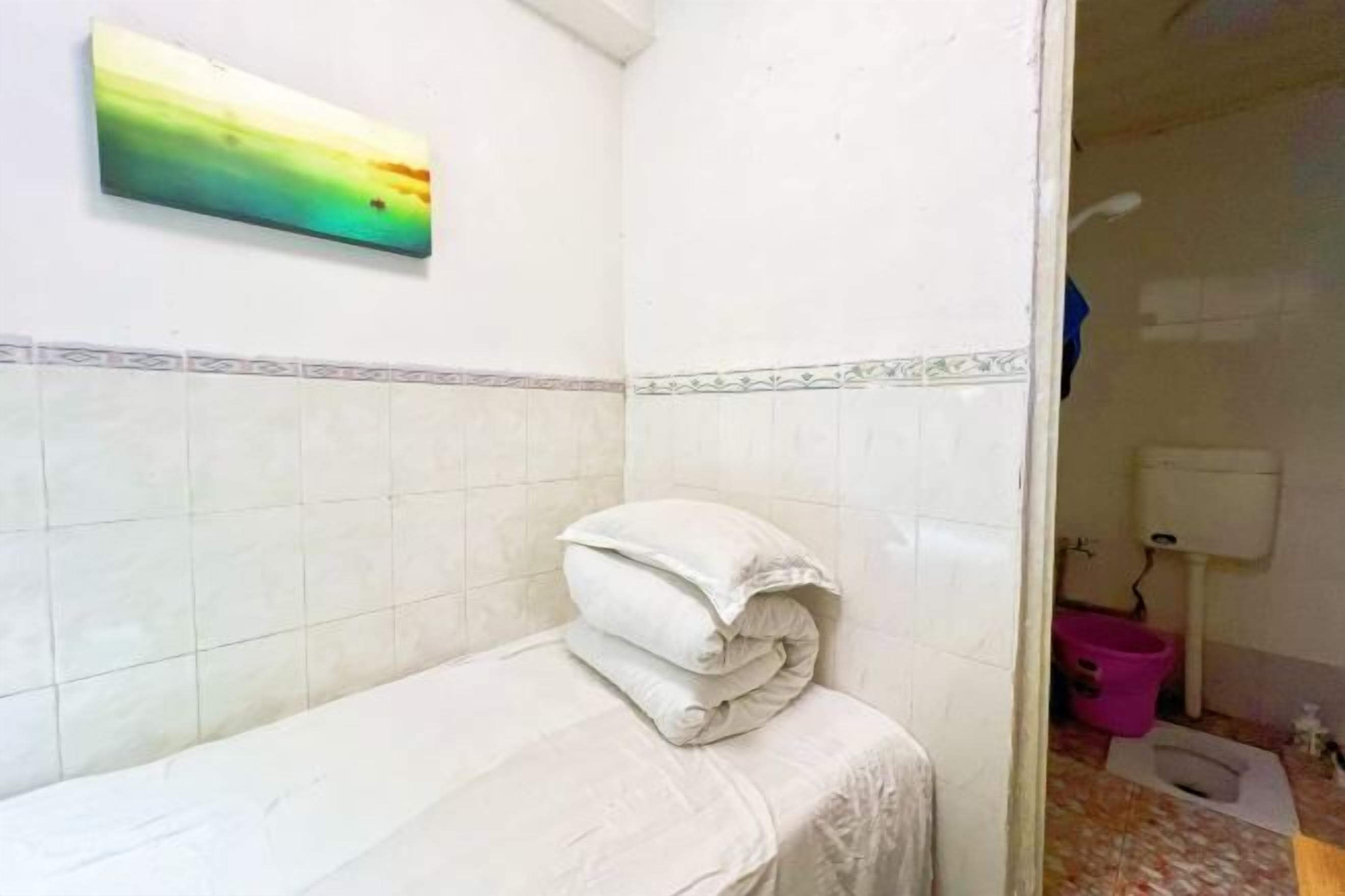 A small bathroom with white tiles, a towel on the floor, and a pink bucket.