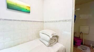 A small bathroom with white tiles, a towel on the floor, and a pink bucket.
