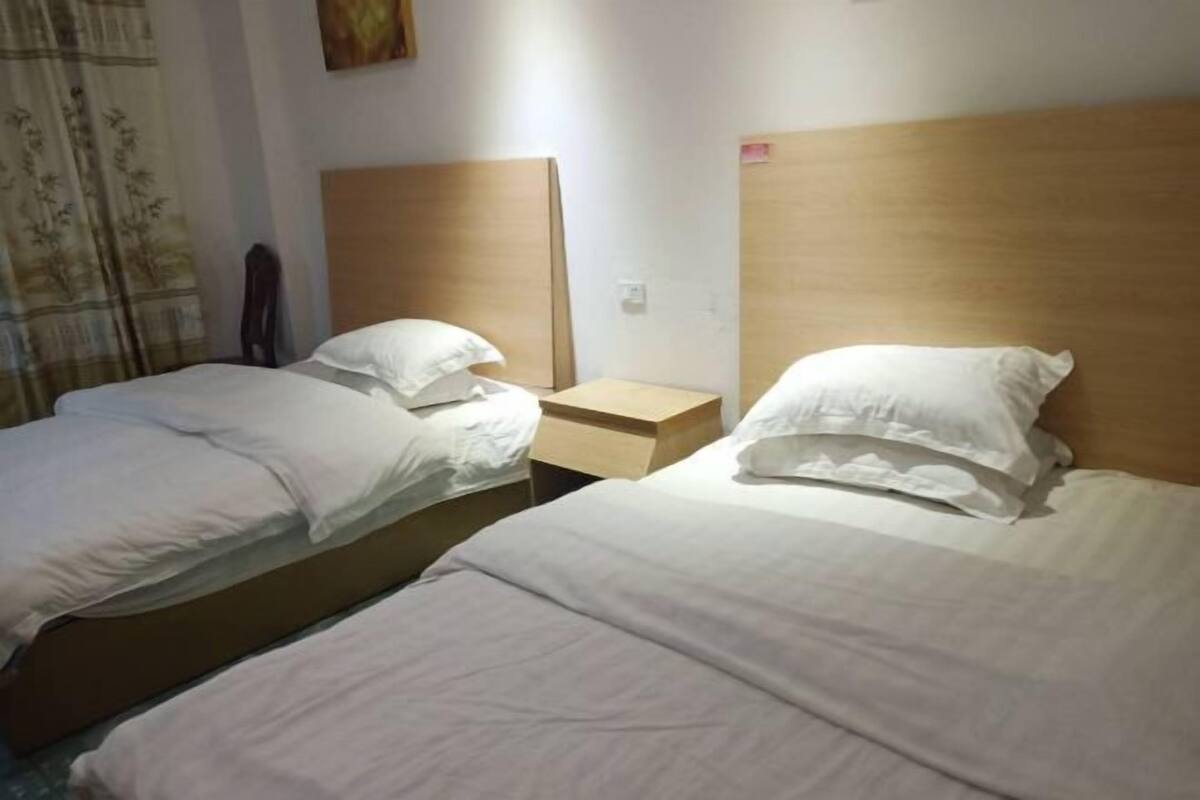 Hotellihuone, jossa on kaksi erillistä sänkyä, puiset päätyosat, valkoiset vuodevaatteet, yöpöytä ja seinälle kiinnitetty taideteos.