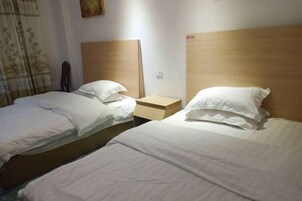 Una habitación de hotel con dos camas individuales, cabeceros de madera, ropa de cama blanca, una mesita de noche y una obra de arte colgada en la pared.