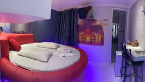 Una habitación con un sofá cama rojo, un pequeño comedor con una mesa y sillas, y un televisor montado en la pared.