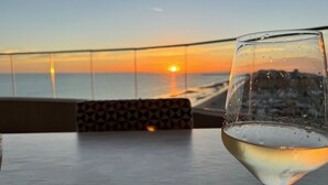 A glass of white wine on a table with a view of the sunset over the ocean. - Amazing brand new 2BD/2Bath Penthouse Condo overlooking the beach. (Puerto Peñasco)