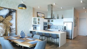 A modern kitchen with a central island, bar stools, and a dining area with a wooden table and chairs. - Amazing brand new 2BD/2Bath Penthouse Condo overlooking the beach. (Puerto Peñasco)