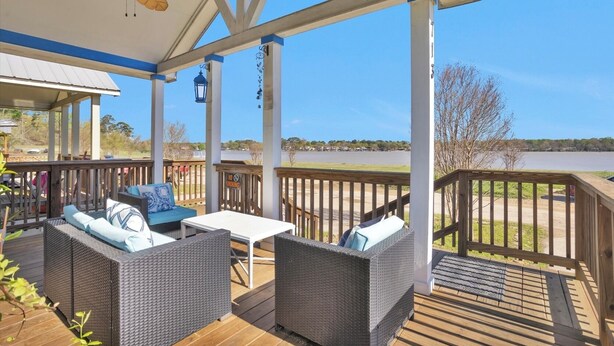 Eine überdachte Terrasse im Freien mit Korbmöbeln, einem Tisch und Blick auf einen See.