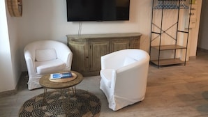 Una sala de estar con dos sillones blancos, un aparador de madera, un televisor y una estantería metálica.