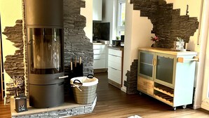 A modern living room with a stone wall, a fireplace, a kitchen area, and a white rug.