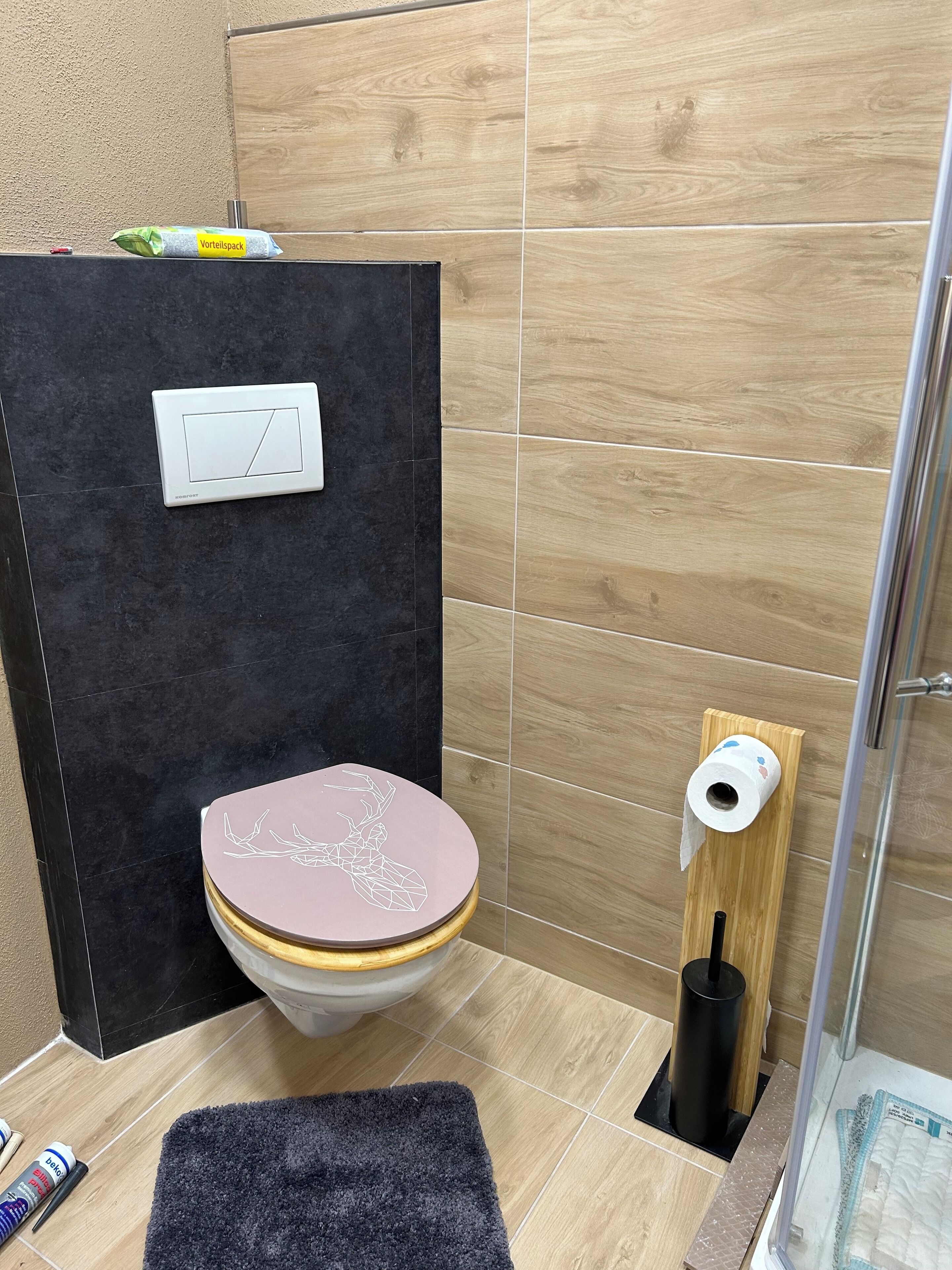 A bathroom with a modern design, featuring a toilet with a geometric pattern on the lid, a black wall, and a wooden floor.