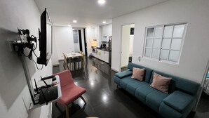 A modern living room with a teal sofa, a red chair, a dining table, and a kitchen area in the background. - #Apt#Rent#Cali#Imbanaco#Tequendama#Colores#SanFernando#Travel#Colombia#Vacation (Cali)