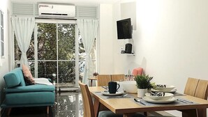 A modern living room with a teal sofa, a wooden dining table set with plates, a coffee maker, and a TV on the wall. - #Apt#Rent#Cali#Imbanaco#Tequendama#Colores#SanFernando#Travel#Colombia#Vacation (Cali)