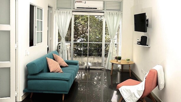 A modern living room with a teal sofa, a pink chair, a small round table with a plant, and a mounted TV. - #Apt#Rent#Cali#Imbanaco#Tequendama#Colores#SanFernando#Travel#Colombia#Vacation (Cali)