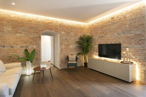 Un salon avec un mur en briques, un téléviseur à écran plat, un canapé, une table basse et une plante en pot.