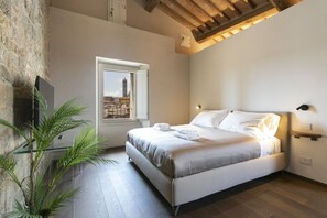 Une chambre à coucher avec un lit, une fenêtre donnant sur la ville, une plante et un plafond en bois.