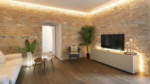 A living room with a brick wall, a flat-screen TV, a sofa, a coffee table, and a potted plant. - PALAZZO RINUCCINI - TORRE apartment (Siena)