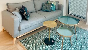 A modern living room with a grey sofa, patterned rug, and a glass table. - Large 1 bedroom -Center terrace parking (Luxembourg City)