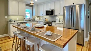 A modern kitchen with white cabinets, stainless steel appliances, and a wooden island with bar stools.