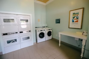 A laundry room with stacked washer and dryer units, a table with a lamp, and a framed picture on the wall. - Orlando | Compact Disney Retreat | Pool + Spa (Lake Buena Vista)