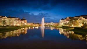 A tranquil lakeside scene with a fountain, reflecting the surrounding buildings and a clear sky. - Orlando | Compact Disney Retreat | Pool + Spa (Lake Buena Vista)