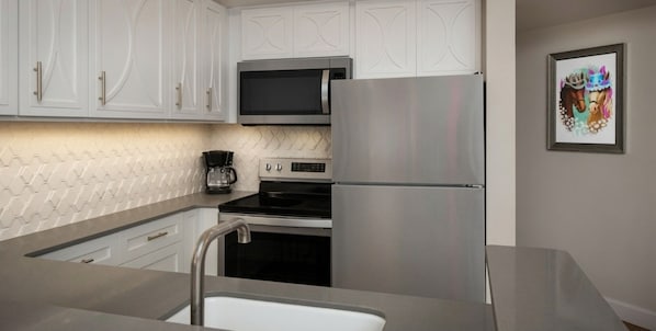 A modern kitchen with stainless steel appliances, white cabinetry, and a coffee maker.