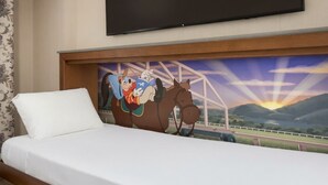 Habitación de hotel con una cama, un televisor montado en la pared y un mural de un personaje de dibujos animados en la cabecera.