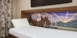 A hotel room with a bed, a television mounted on the wall, and a mural of a cartoon character on the headboard.