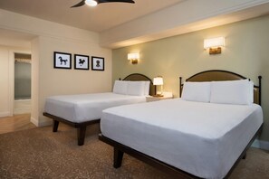 A hotel room with two single beds, a nightstand with a lamp, and three framed pictures on the wall.