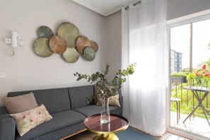 A living room with a grey sofa, decorative wall art, a vase with greenery, and a view through a window.
