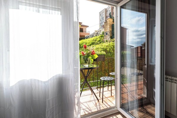 A room with a sliding glass door leading to an outdoor area with a table and chairs, a potted plant, and a view of buildings and greenery.