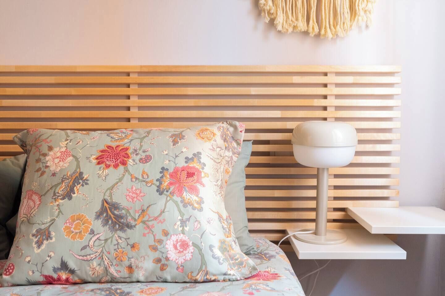 Una cama con un cojín estampado con motivos florales y una mesita de noche con una lámpara.