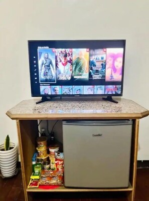 Un téléviseur posé sur un meuble en bois, avec un petit réfrigérateur en dessous.