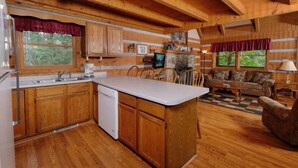 A cabin interior with wooden floors, a kitchen with wooden cabinets, a dining area with a table and chairs, and a living room with a sofa and a lamp. - Paradise #3111 (Gatlinburg)