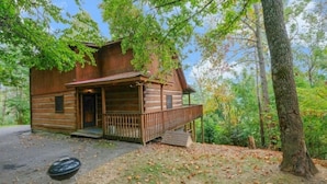 A rustic cabin with a porch, surrounded by trees and a gravel driveway. - Paradise #3111 (Gatlinburg)