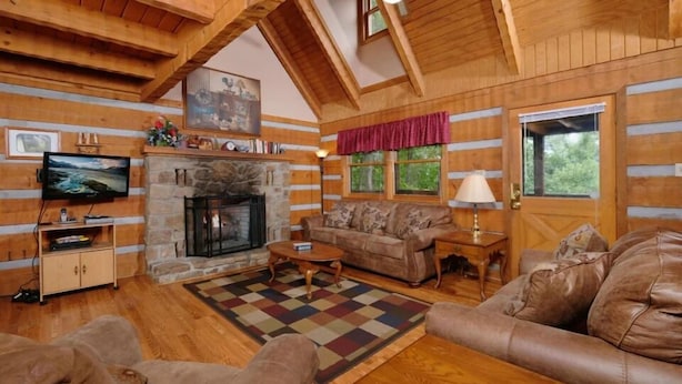 A cozy log cabin interior with a stone fireplace, wooden walls, a television, and a comfortable seating area. - Paradise #3111 (Gatlinburg)