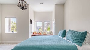 Ein Schlafzimmer mit einem großen Bett, Blick durch ein Fenster nach draußen und einer Deckenleuchte.