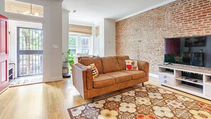 Ein Wohnzimmer mit Backsteinwand, einem braunen Sofa, einem Fernseher und einem gemusterten Teppich.