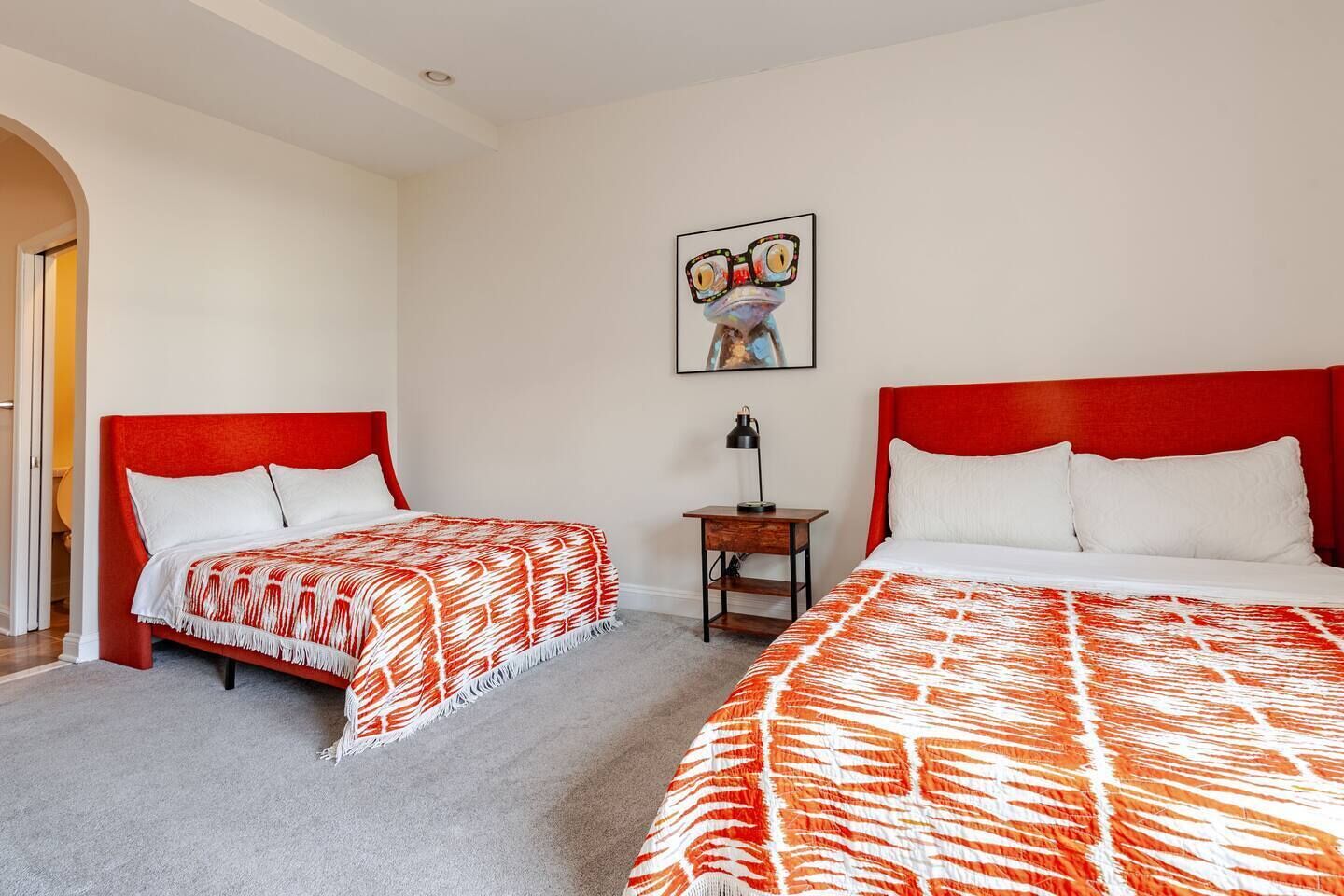 A hotel room with two beds, a nightstand, a lamp, and a framed picture on the wall.