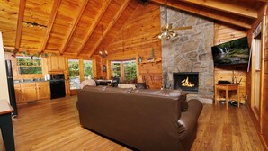 A spacious living room with a stone fireplace, wooden ceiling, and a flat-screen TV mounted above it. - Country Romance #1279 (Sevierville)