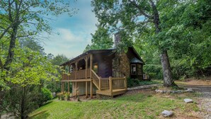 A rustic cabin with a wooden deck and stone chimney, surrounded by lush greenery. - Country Romance #1279 (Sevierville)