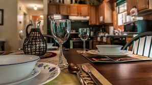 A dining table set with plates, bowls, wine glasses, and cutlery in a kitchen with wooden cabinets and a microwave. - Country Romance #1279 (Sevierville)
