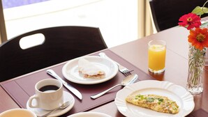 Una mesa de desayuno con platos de comida, un vaso de jugo de naranja, una taza de café y un florero con flores.