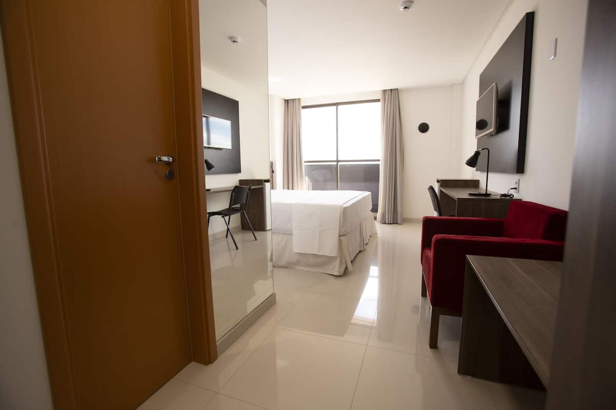 Une chambre d’hôtel avec un lit, un bureau, une chaise, une télévision et une grande fenêtre.