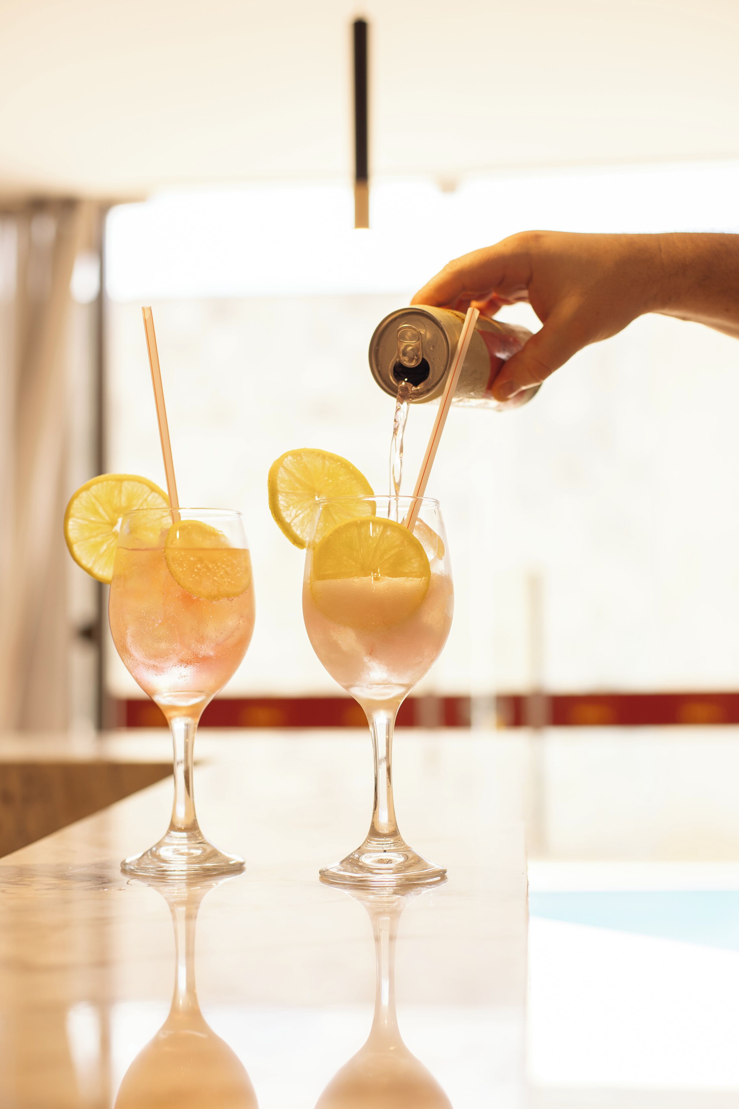 Two glasses of a beverage with lemon slices on a reflective surface.