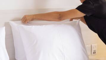 Una persona acomodando un almohadón blanco sobre una cama con cabecera de madera.