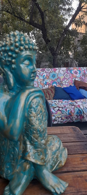 A statue of a seated figure with intricate carvings, placed on a wooden surface. In the background, there is a colorful sofa with a floral pattern and a brown cushion. - Pequeña Estacion B&B (Mendoza)
