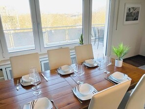 A dining table set for six with white plates, glasses, and cutlery, large windows with a view of trees, and a small potted plant on the table. - Penthouse in Center - Parking&Terrace (Luxembourg City)