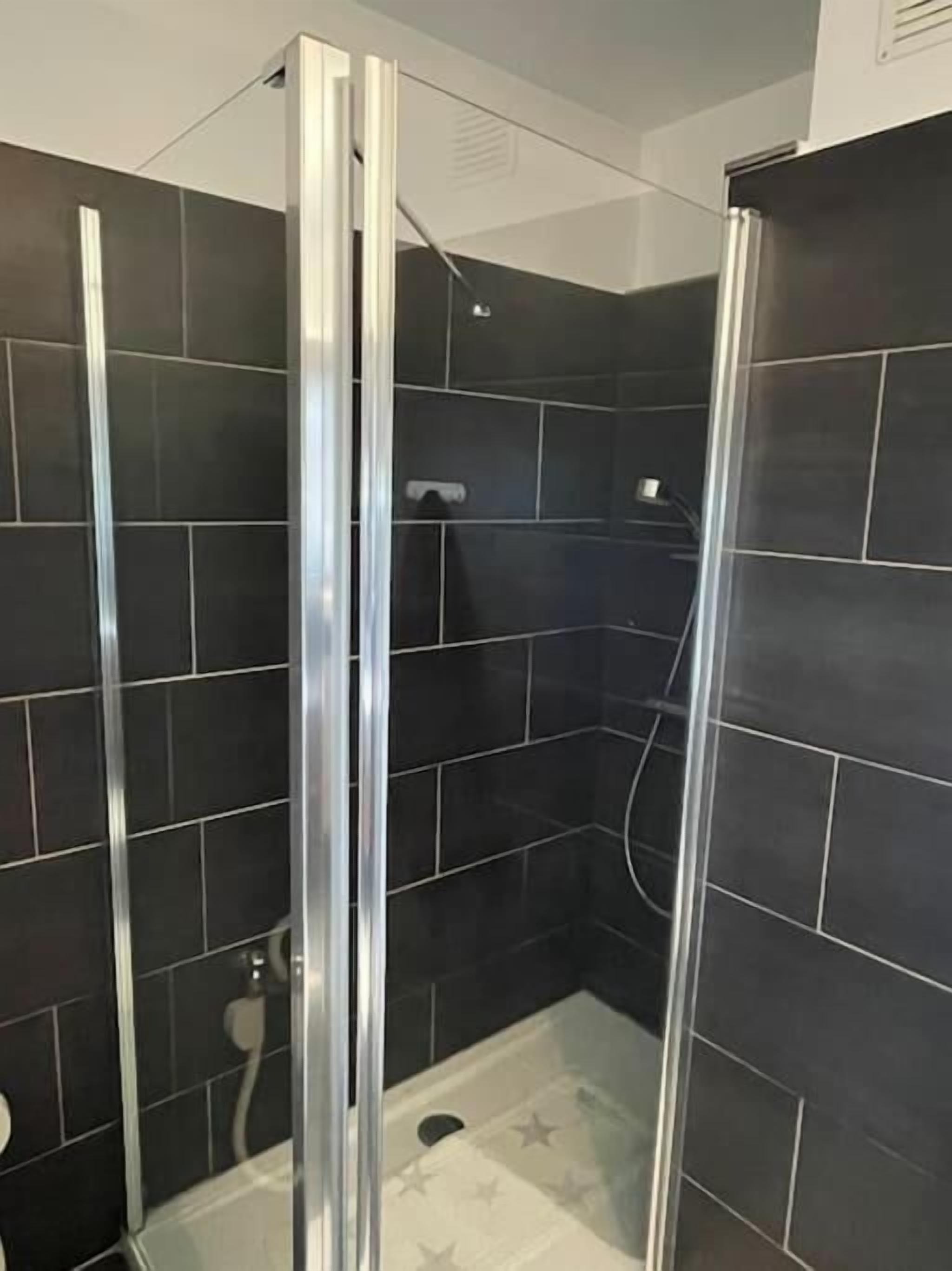 A shower area with dark tiles, a glass door, and a star-patterned shower floor.