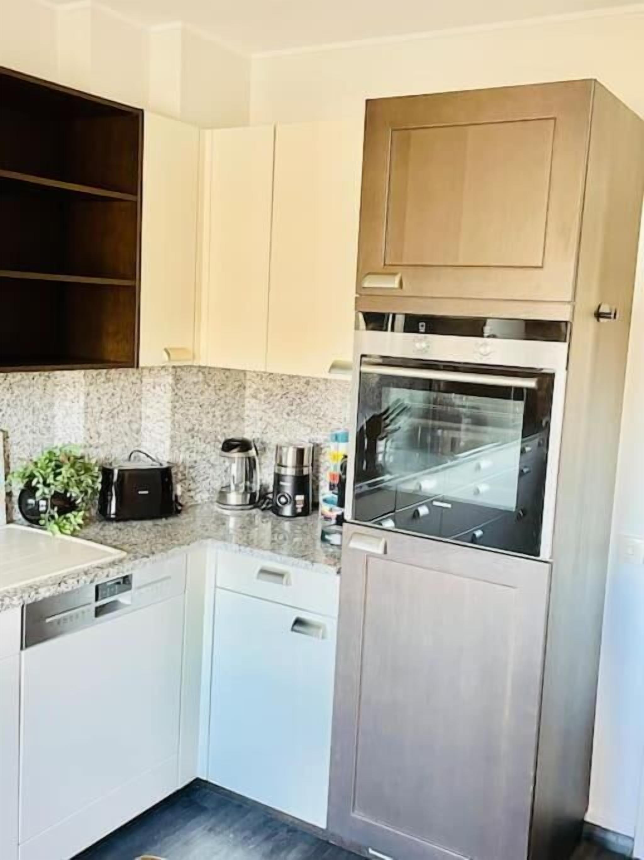 A modern kitchen with white cabinets, a stainless steel refrigerator, and a built-in oven.