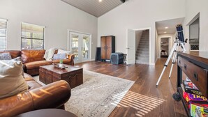 Un salon spacieux avec un canapé en cuir, une table basse et un grand tapis. On y trouve également un meuble en bois et un télescope posé sur un chariot.