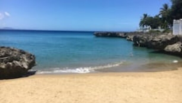 Ein Strand mit klarem türkisblauem Wasser, Sandstrand und Felsen.