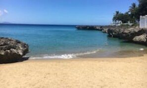 A beach with clear turquoise water, sandy shore, and rocky outcrops.