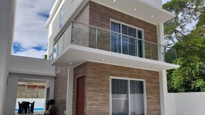 Ein modernes, zweistöckiges Haus mit Balkon, großen Schiebeglastüren und einem sichtbaren Sitzbereich im Freien.